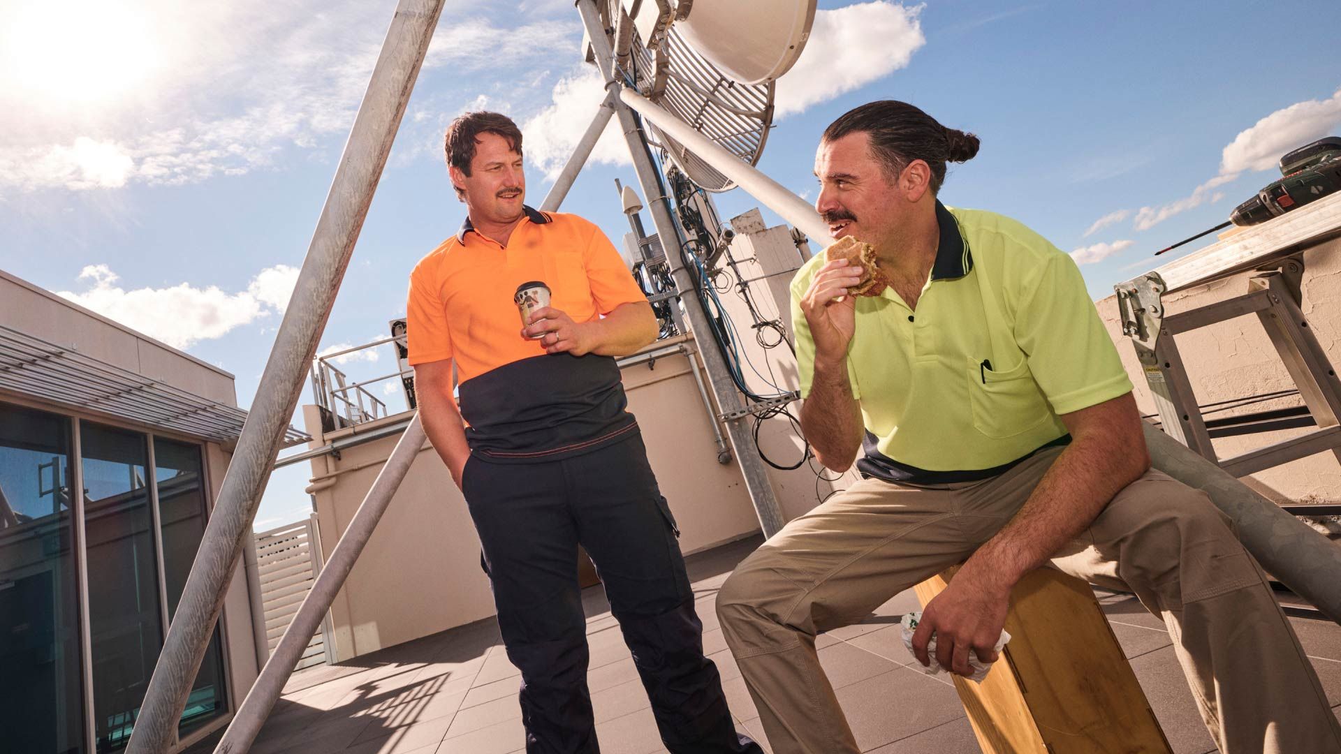 Photo of two cheerful tradesmen, having a lunch break on a roof top.