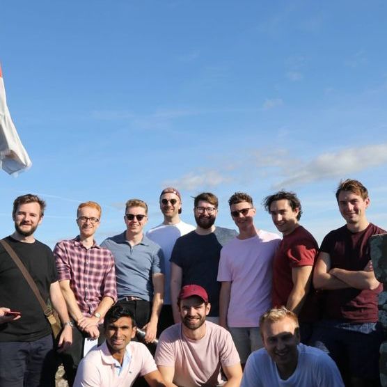 Group photo of young men in t-shirts posing for a photo beneath a blue sky.